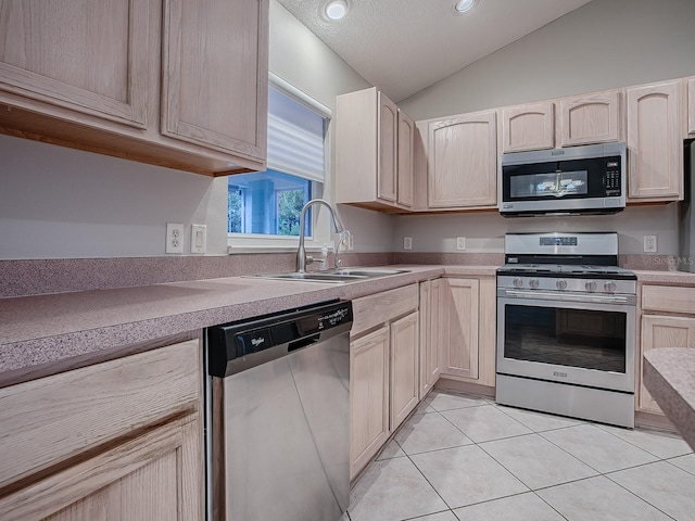 kitchen featuring stainless steel appliances, vaulted ceiling, sink, light brown cabinets, and light tile patterned floors