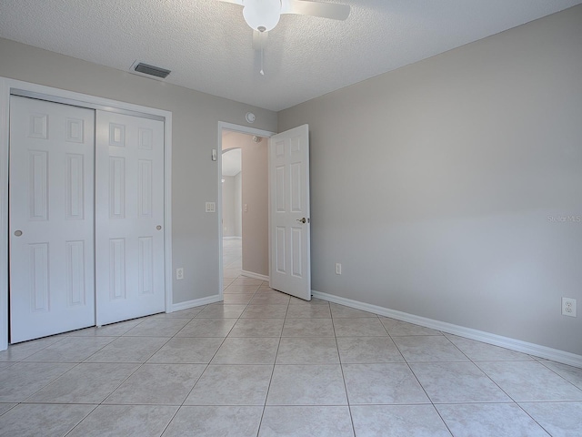 unfurnished bedroom with ceiling fan, light tile patterned floors, a textured ceiling, and a closet