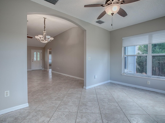 empty room featuring ceiling fan with notable chandelier, light tile patterned floors, a textured ceiling, and plenty of natural light