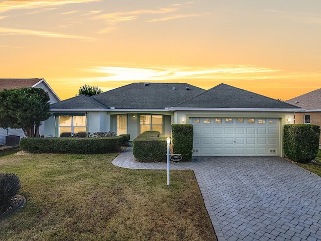 single story home with a lawn, central AC unit, and a garage