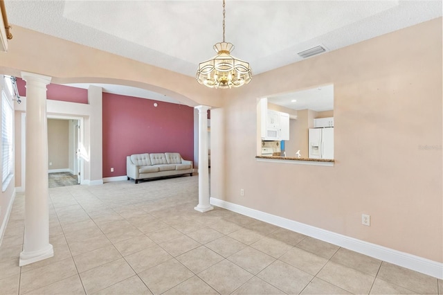 tiled empty room featuring ornate columns, a textured ceiling, and a notable chandelier