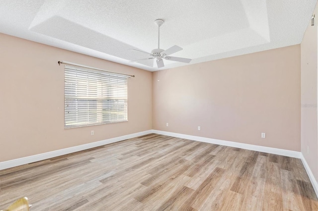 spare room featuring a raised ceiling, ceiling fan, light hardwood / wood-style flooring, and a textured ceiling