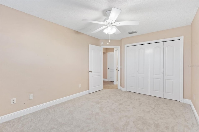 unfurnished bedroom with ceiling fan, light colored carpet, a textured ceiling, and a closet