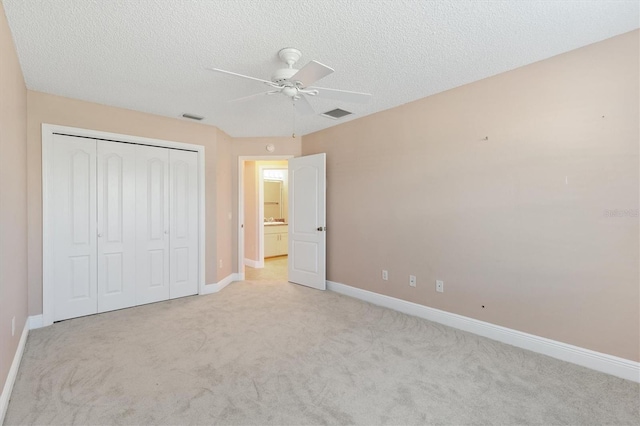 unfurnished bedroom with a textured ceiling, ceiling fan, light carpet, and a closet