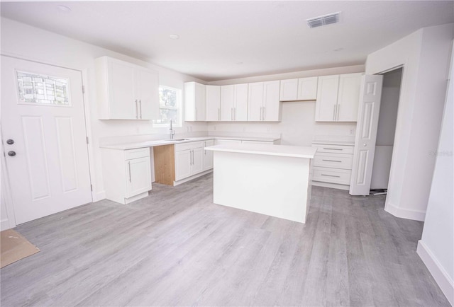 kitchen with sink, light hardwood / wood-style flooring, white cabinets, and a center island