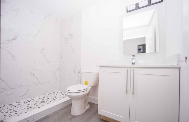 bathroom featuring hardwood / wood-style flooring, toilet, vanity, and a tile shower