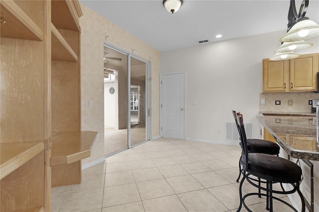 kitchen featuring light stone countertops, light brown cabinets, light tile patterned floors, and hanging light fixtures