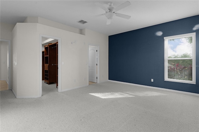 unfurnished bedroom with ceiling fan, a walk in closet, light carpet, and a closet