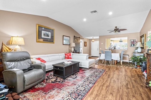 living room with hardwood / wood-style flooring, a barn door, ceiling fan, and vaulted ceiling