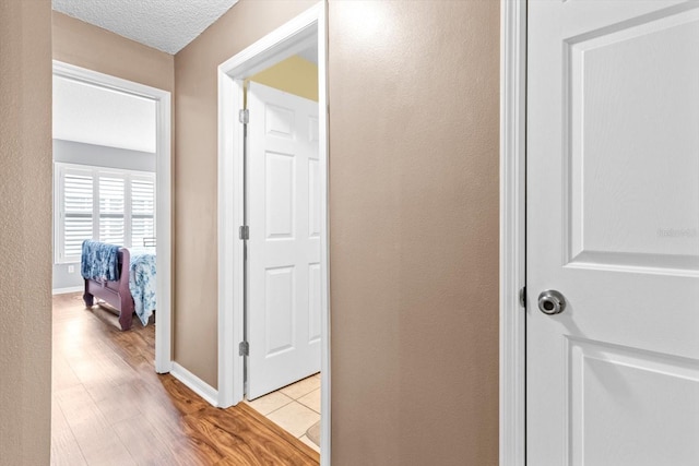 hallway with a textured ceiling and light hardwood / wood-style flooring