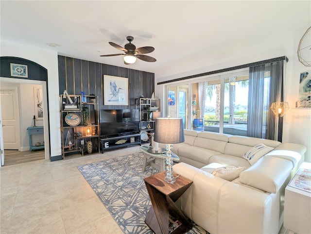 tiled living room with ceiling fan and wood walls