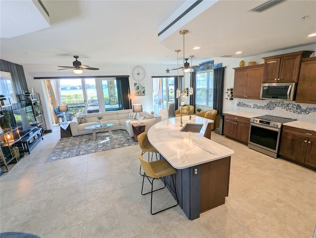 kitchen featuring a kitchen bar, appliances with stainless steel finishes, backsplash, a kitchen island with sink, and sink