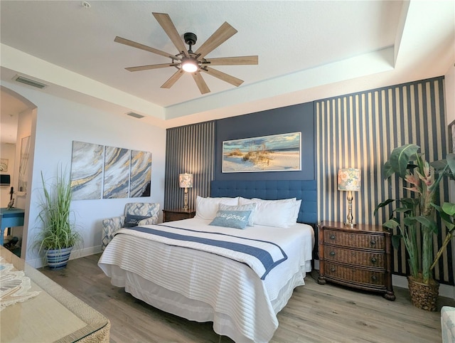 bedroom with hardwood / wood-style floors, ceiling fan, and a raised ceiling