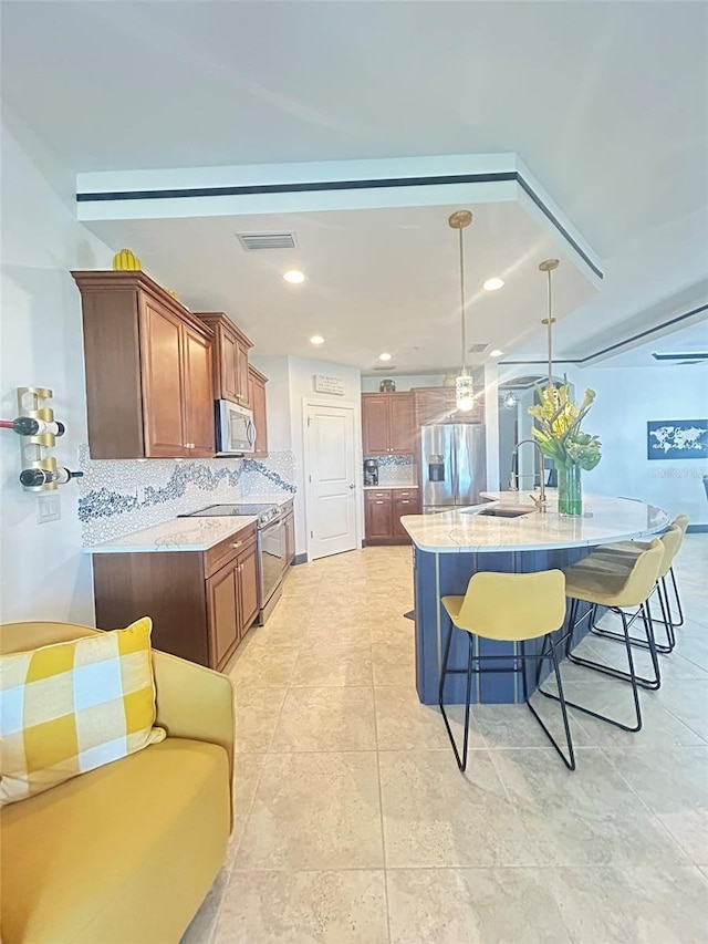 kitchen featuring decorative backsplash, a breakfast bar area, appliances with stainless steel finishes, a sink, and visible vents