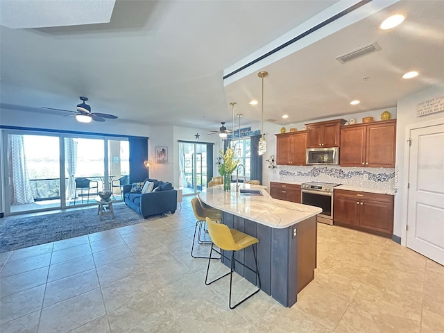 kitchen featuring decorative backsplash, a breakfast bar area, stainless steel appliances, ceiling fan, and a sink