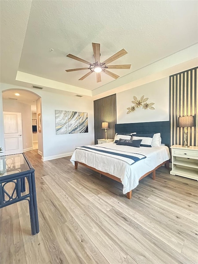 bedroom featuring arched walkways, visible vents, wood finished floors, and a tray ceiling
