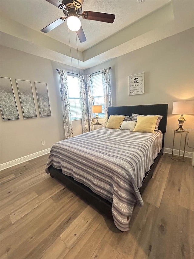 bedroom with wood finished floors, ceiling fan, a tray ceiling, and baseboards