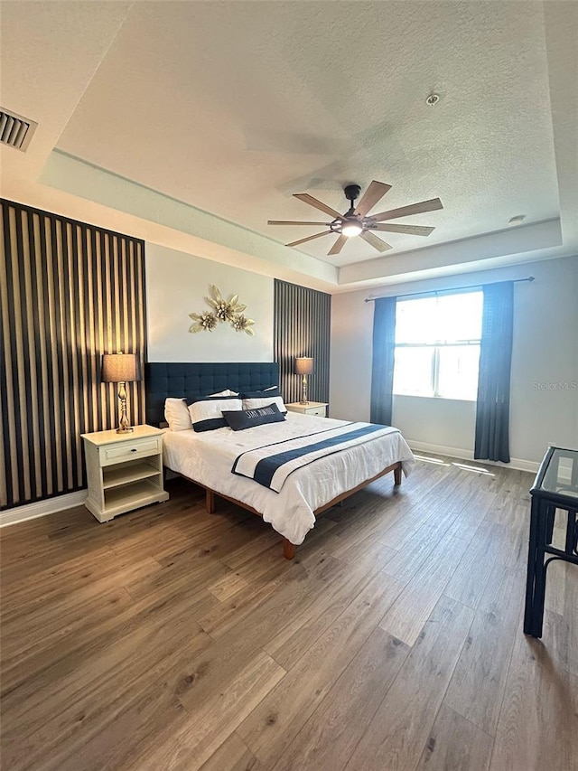 bedroom with wood finished floors, baseboards, visible vents, a textured ceiling, and a tray ceiling