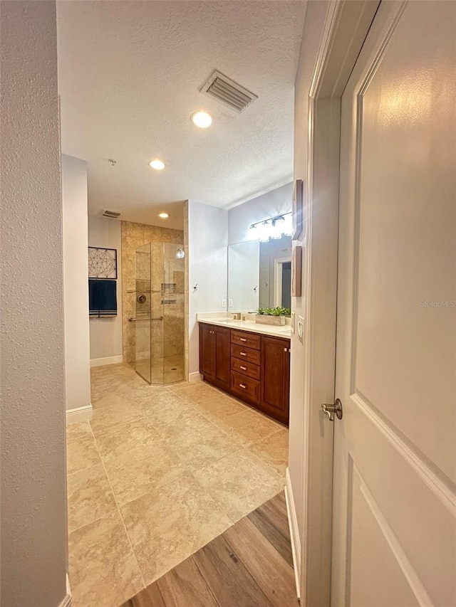 full bath with a textured ceiling, double vanity, visible vents, recessed lighting, and a walk in shower