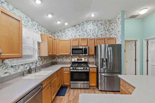 kitchen featuring wallpapered walls, vaulted ceiling, stainless steel appliances, and a sink