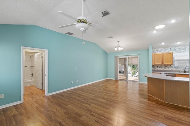 kitchen with light countertops, open floor plan, vaulted ceiling, wood finished floors, and ceiling fan with notable chandelier