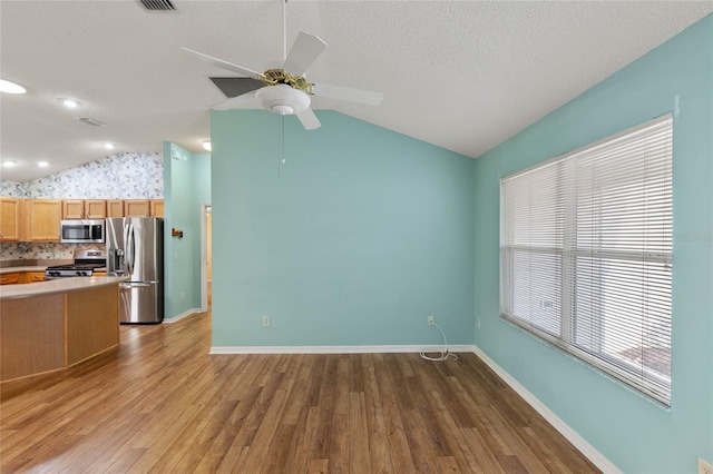 interior space with lofted ceiling, baseboards, a textured ceiling, and light wood finished floors