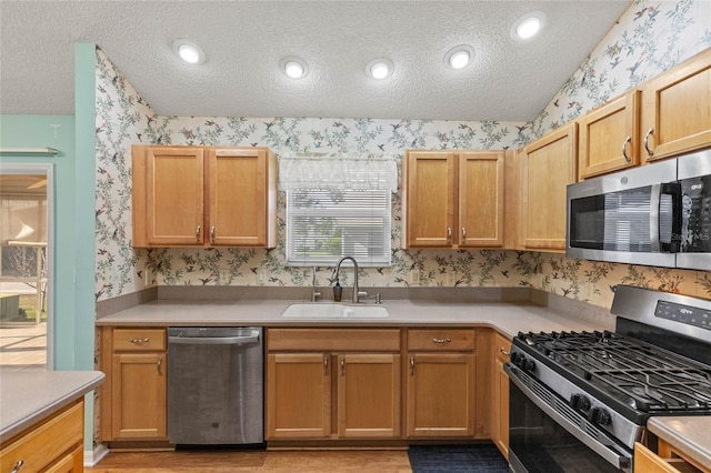 kitchen with wallpapered walls, a textured ceiling, appliances with stainless steel finishes, and a sink