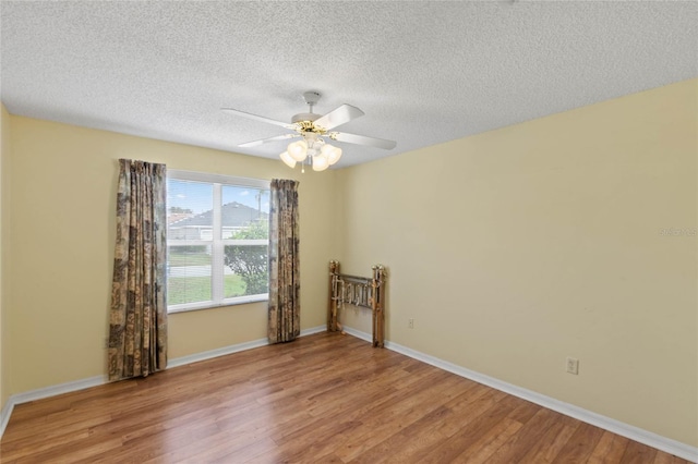 spare room featuring light wood-style floors, a textured ceiling, baseboards, and a ceiling fan