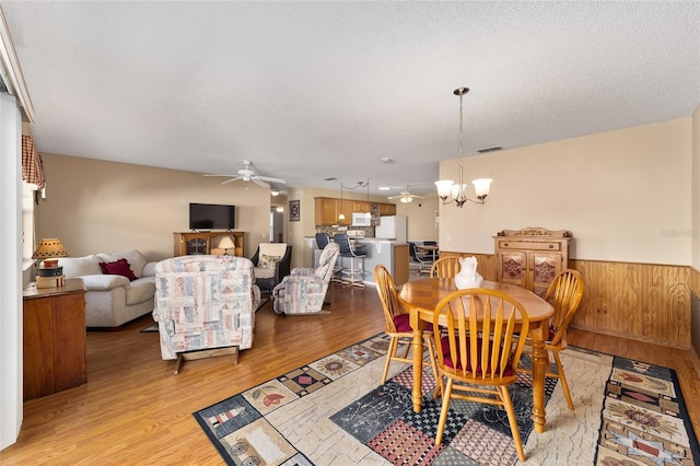 dining space featuring a textured ceiling, light hardwood / wood-style flooring, and ceiling fan with notable chandelier