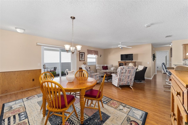 dining room featuring ceiling fan with notable chandelier, a textured ceiling, wood walls, and hardwood / wood-style flooring