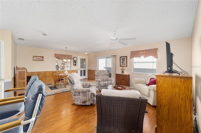 living room with a textured ceiling, light hardwood / wood-style flooring, wooden walls, and ceiling fan with notable chandelier