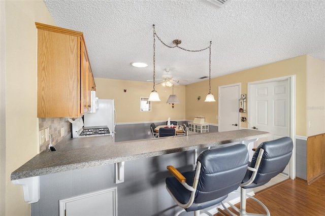 kitchen with kitchen peninsula, a textured ceiling, light hardwood / wood-style floors, a breakfast bar, and decorative backsplash