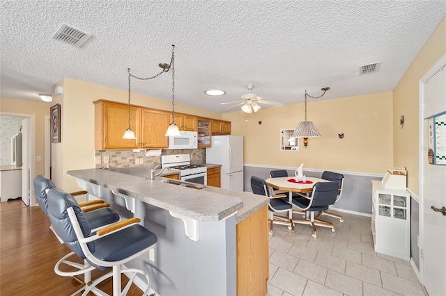 kitchen with white appliances, pendant lighting, a breakfast bar area, and kitchen peninsula