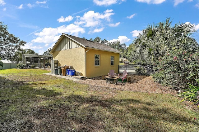 view of side of home featuring a yard, an outdoor fire pit, and a lanai