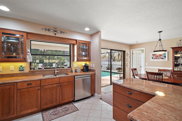 kitchen with pendant lighting, dishwasher, sink, light tile patterned floors, and light stone counters