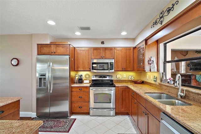 kitchen with light stone countertops, appliances with stainless steel finishes, a textured ceiling, sink, and light tile patterned flooring