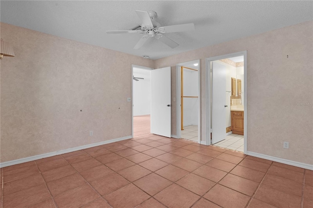 unfurnished bedroom featuring ceiling fan, light tile patterned floors, a textured ceiling, and ensuite bath