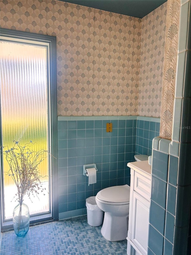 bathroom with a wealth of natural light, vanity, tile walls, tile patterned flooring, and toilet