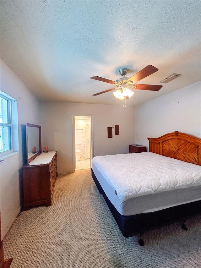 bedroom featuring ceiling fan, light colored carpet, a textured ceiling, and connected bathroom