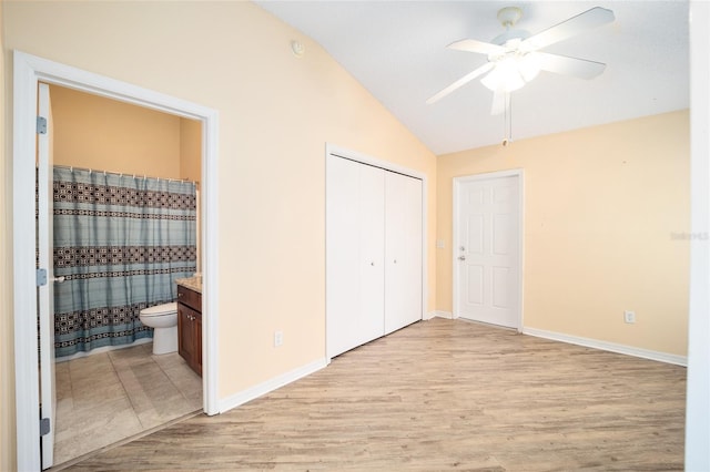 unfurnished bedroom featuring ceiling fan, ensuite bathroom, lofted ceiling, and light wood-type flooring