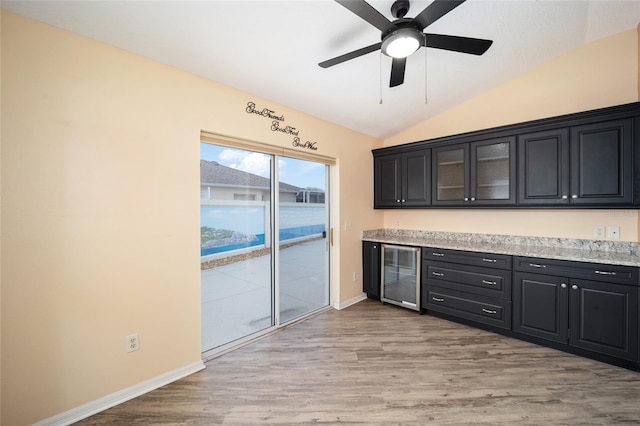 kitchen featuring wine cooler, ceiling fan, vaulted ceiling, light stone counters, and light hardwood / wood-style flooring