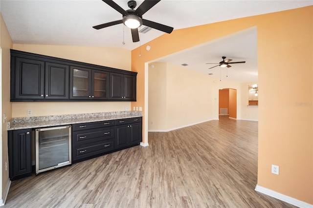 kitchen with wine cooler, light hardwood / wood-style floors, ceiling fan, vaulted ceiling, and light stone counters