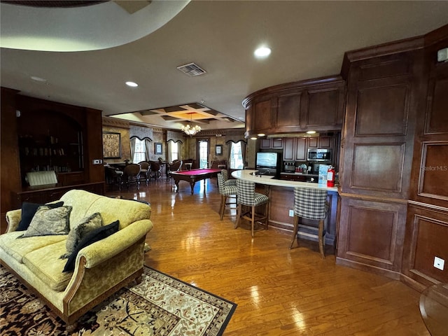 living room with light wood-type flooring, a raised ceiling, wooden walls, an inviting chandelier, and billiards