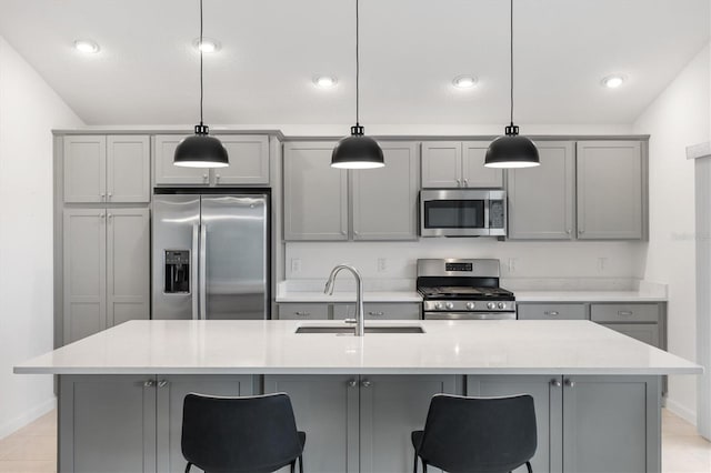 kitchen with gray cabinetry, sink, decorative light fixtures, a center island with sink, and appliances with stainless steel finishes