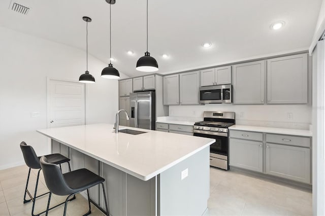 kitchen featuring appliances with stainless steel finishes, gray cabinetry, sink, decorative light fixtures, and an island with sink