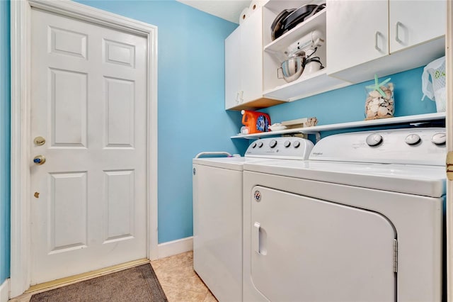 clothes washing area featuring cabinets, light tile patterned flooring, and washing machine and clothes dryer