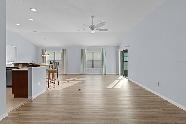 unfurnished living room featuring a textured ceiling, vaulted ceiling, ceiling fan, sink, and light hardwood / wood-style flooring