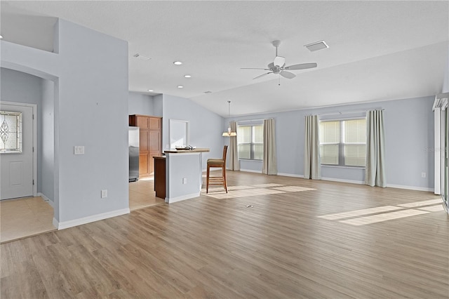 unfurnished living room featuring ceiling fan with notable chandelier, light hardwood / wood-style floors, and vaulted ceiling