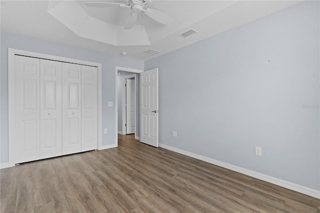 unfurnished bedroom featuring ceiling fan, a raised ceiling, wood-type flooring, and a closet