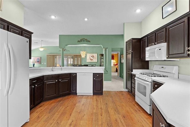 kitchen featuring dark brown cabinetry, sink, hanging light fixtures, light hardwood / wood-style flooring, and white appliances